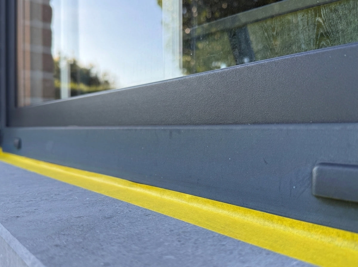Q1 sun-yellow masking tape along a bluestone sill under an anthracite aluminium window frame