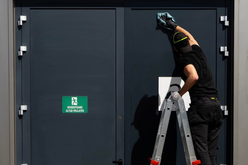 Installer restoring tall anthracite aluminium doors from a stepladder